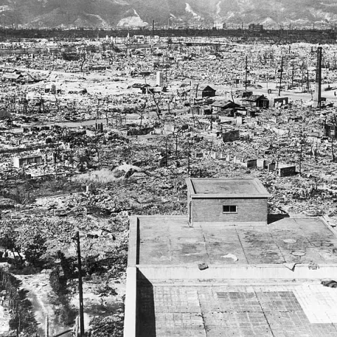 A black and white aerial photograph of Hiroshima after the atomic bomb: a flattened city with a few buildings still standing