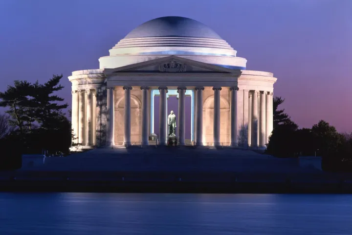 The Jefferson Memorial at dusk, its columns glowing with warm light above the dark water of the Tidal Basin