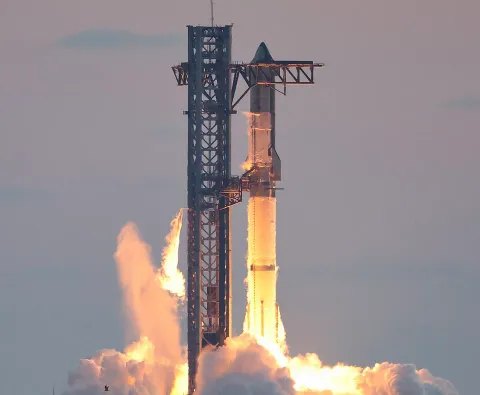A Starship and its Super Heavy booster on the launch tower at dusk, engines lit and clouds of exhaust billowing around the base
